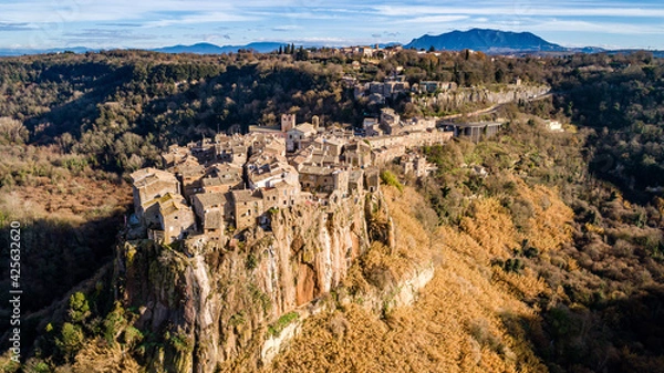 Fototapeta Postcard from Italy. Aerial view of the medieval village of Calcata with its volcanic cliff and the valley of the Treja river with Mount Soratte in the background.