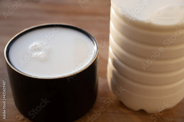Obraz Glass of milk standing on old wooden table. Black glass with white milk. Black glass with white milk on the table