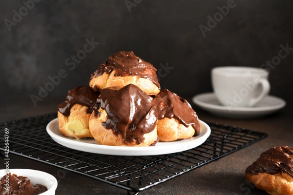Fototapeta Profiteroles with vanilla cream and chocolate sauce with a cup of coffee on the kitchen table.