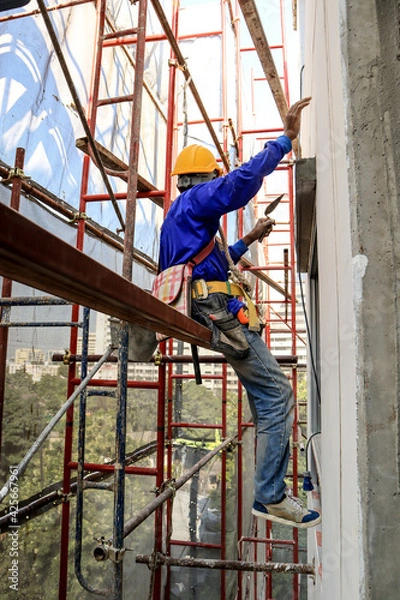 Fototapeta A plasterer stands on a scaffold to plaster the outside of the building.