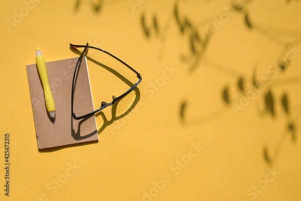 Fototapeta Eye glasses and notepad with pen on yellow top background.