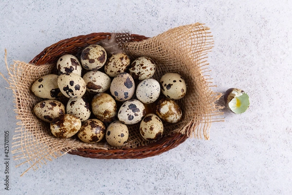 Fototapeta Quail eggs lie on a jute cloth in a beautiful wooden dish. Natural bird feathers are scattered around. Next to it is the shell of a broken egg.. 