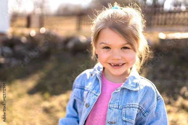 Fototapeta A seven year old girl laughs and rejoices in the spring on the street in a denim jacket.