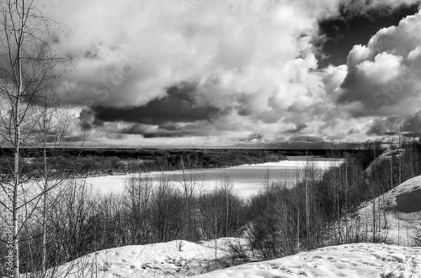 Obraz Winter landscape with a high bank of the river covered with ice, cumulus clouds in the sky,.deep snow cover with footprints, a clear horizon line, monochrome.