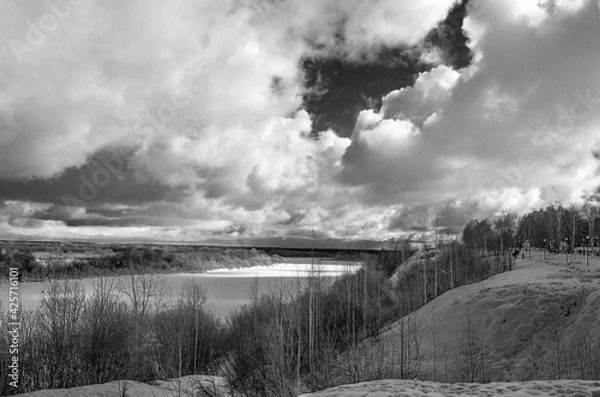 Obraz Winter landscape with a high bank of the river covered with ice, cumulus clouds in the sky,.deep snow cover with footprints, a clear horizon line, monochrome.