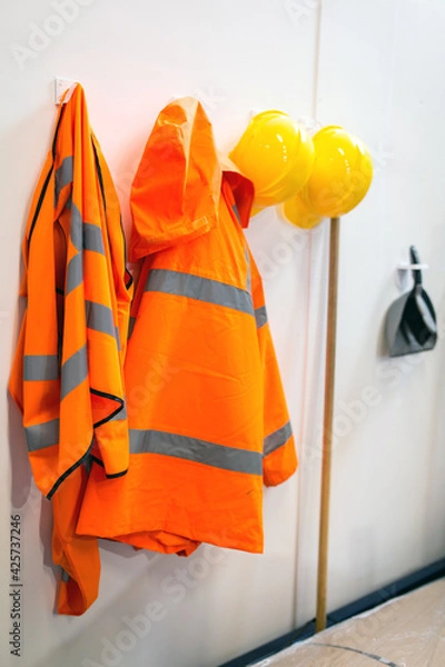 Fototapeta High visibility protective clothing and hard hats hanging up in a warehouse for easy access for the workers. Warehouse, stores, safety gear concept