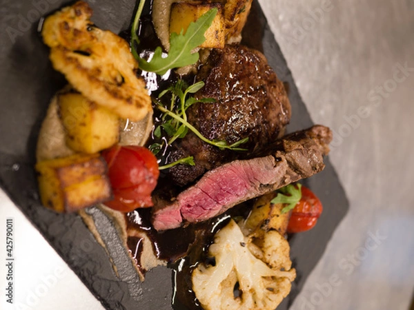 Fototapeta Juicy Beef rump steak from marble beef medium rare with spices and grilled vegetables on black stone plate, close-up.