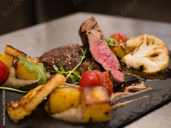 Fototapeta Juicy Beef rump steak from marble beef medium rare with spices and grilled vegetables on black stone plate, close-up.