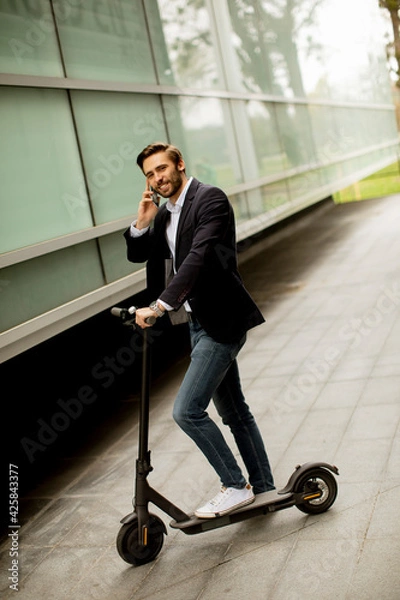 Fototapeta Young businessman using mobile phone  on electric scooter