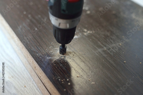 Fototapeta In purple, a man drills a hole in a blank for laminating MDF furniture. MDF furniture assembly concept