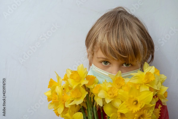 Fototapeta This is a portrait of a boy wearing a medical mask holding a bouquet of yellow flowers.