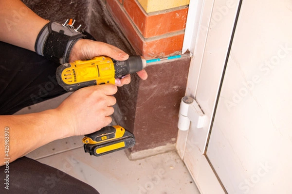 Fototapeta male hands of  construction worker tighten and fix  screws and self-tapping screw  with  electric cordless screwdriver for home improvement and building interior decoration.