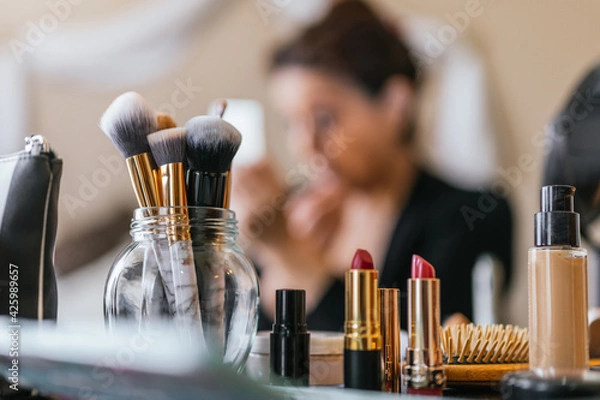 Obraz Lipsticks on a wooden table and in the background a woman putting on makeup
