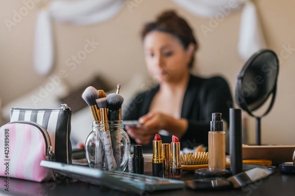 Obraz Lipsticks and makeup brushes on a wooden table, in the background a woman putting on makeup