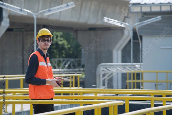 Fototapeta workers at work. Worker checking job with Hand  hold folder  on plant and building background.