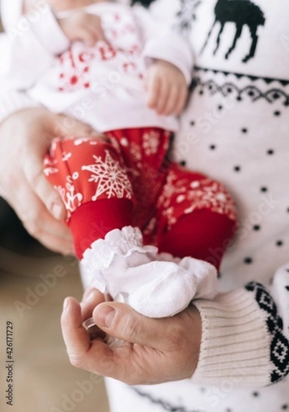 Obraz Dad is holding the baby in his arms. On the hand are small children's legs in stumps. Father and child are dressed in New Year's clothes. The first new year of the child. Baby.
