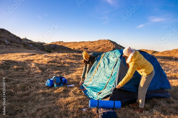 Fototapeta Women building a tent in the mountains, preparing for a camping night.	