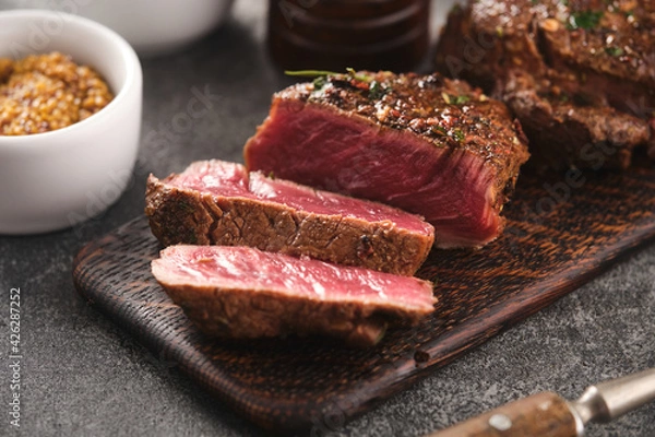 Fototapeta Grilled beef fillet steaks with herbs and spices on wooden board. Two Fillet mignon. Fillet of beef.