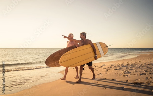 Fototapeta Two senior surfers with surfboard having fun on empty remote beach enjoying retirement lifestyle