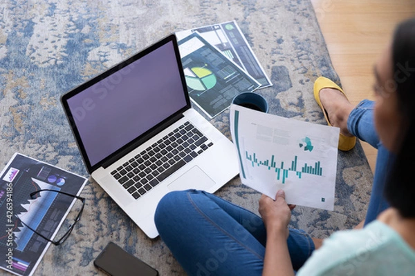 Fototapeta Mixed race gender fluid man working at home sitting on floor using laptop, copy space screen