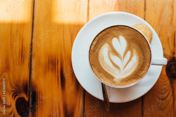Obraz Flat lay. A cup of cappuccino with foam on a wooden table in a light cafe. pattern