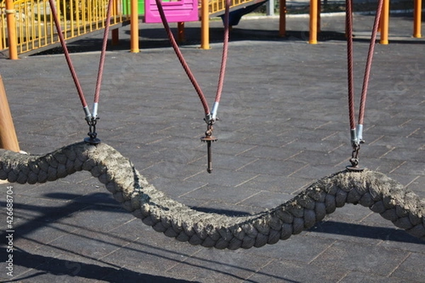Fototapeta A Strong rope swing with broken suspension at a playground at noon.