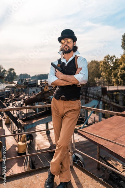 Fototapeta Steampunk. A hero on a river barge surrounded by steel mechanisms. A man with a weapon.