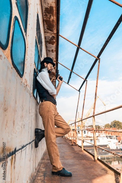 Fototapeta Steampunk. A hero on a river barge surrounded by steel mechanisms. A man with a weapon.