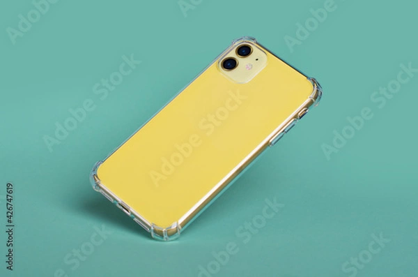 Obraz Yellow iPhone 11 in clear silicone case falls down isolated on green background back view. Phone case mockup