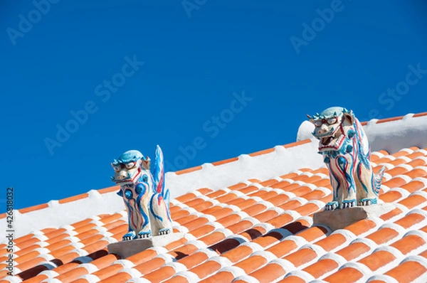 Fototapeta Two highly colored shisa statues, male and female, used as protection, on top of the red roof. Contrasting with the super blue sky in the background. Typical Okinawa scene.