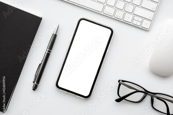 Fototapeta Smartphone with blank mockup screen is on top of white office desk table with supplies. Top view with copy space, flat lay.