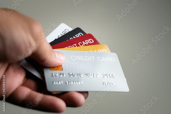 Fototapeta Multiple colors credit card in hand use paying for shopping in store and online, payment via bank and financial concept 