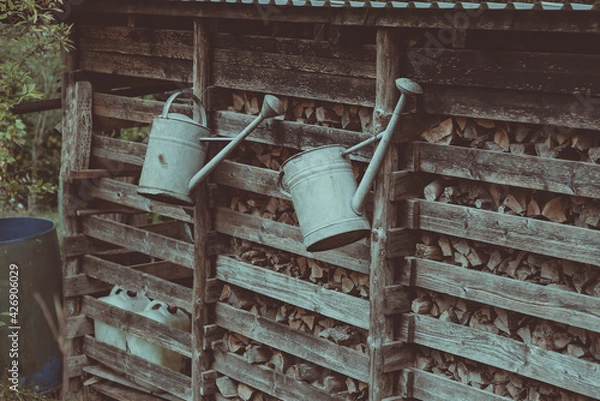 Fototapeta two watering cans hang on the fence