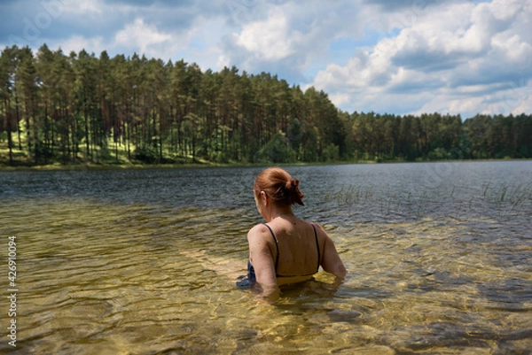 Obraz Dziewczyna wypoczywająca nad czystym jeziorem w promieniach letniego słońca, w tle zielony las.
