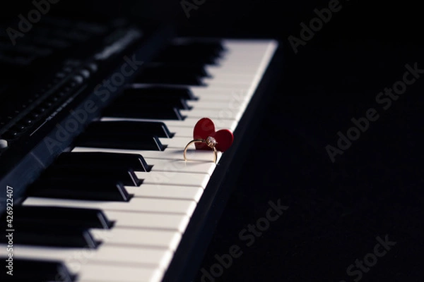 Obraz Engagement ring and small heart on a piano with dark background