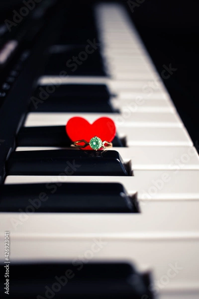 Obraz Engagement ring and small heart on a piano with dark background