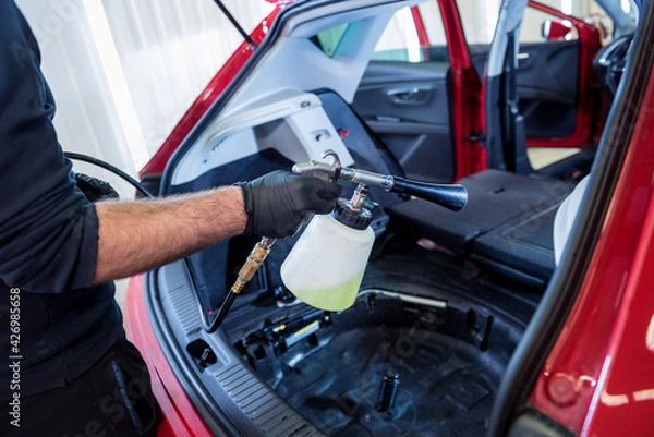 Fototapeta A car service worker cleans interiror with a special foam generator