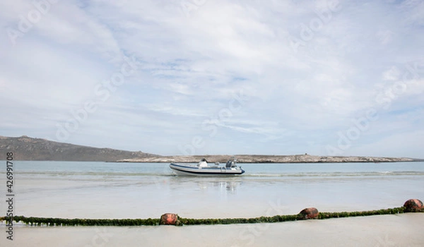 Fototapeta Langebaan Lagoon, South Africa. A Beautiful tourist destination with rocky coastline and speed boat on shore with fishing net.