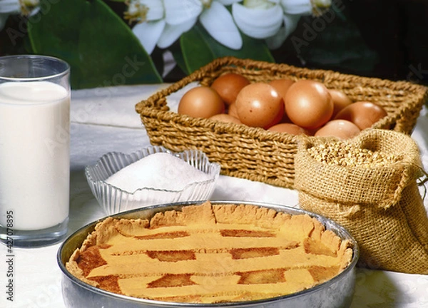 Fototapeta Gluten-free Neapolitan Pastiera with the ingredients in a cup full of sugar, a basket of fresh eggs, a bottle of milk and a hemp bag full of buckwheat