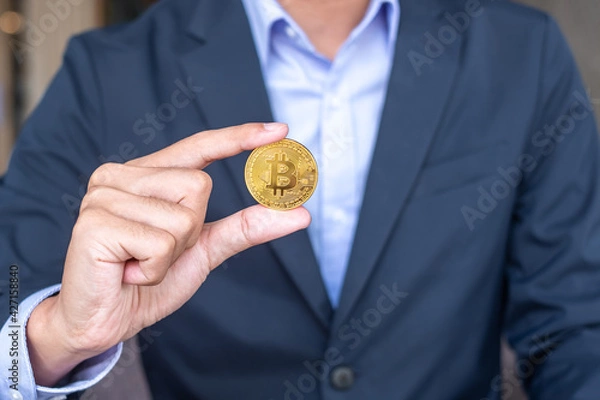 Fototapeta Businessman hand holding golden Bitcoin (BTC) cryptocurrency, Crypto is Digital Money within the blockchain network, is exchanged using technology and online internet exchange. Financial concept