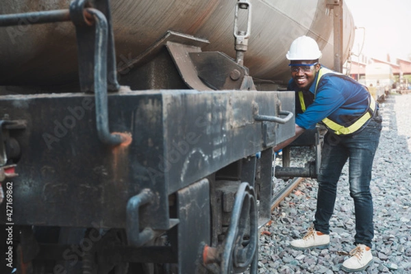 Fototapeta African machine engineer technician wearing a helmet, groves and safety vest is using a wrench to repair the train