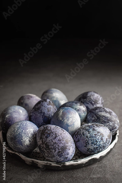 Fototapeta organic Easter eggs on a dark background, hand-painted with natural blueberries, lie in a clay cup on a stone table. Easter concept.