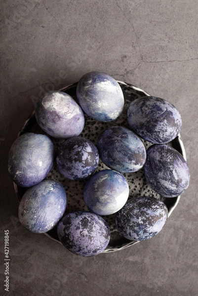 Fototapeta organic Easter eggs close-up, hand-painted with natural blueberries, lie in a clay cup on a stone table. Easter concept. flat lay