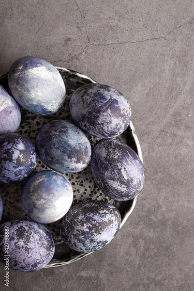 Fototapeta organic Easter eggs close-up, hand-painted with natural blueberries, lie in a clay cup on a stone table. Easter concept. flat lay
