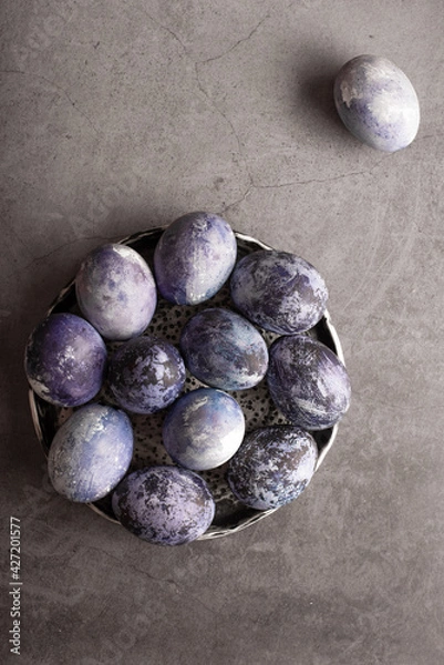 Fototapeta marble Easter eggs on a dark background, hand-painted with natural blueberries, lie in a clay cup on a stone table. Easter preparation concept.