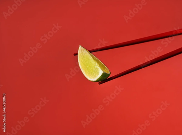 Obraz Red Chinese chopsticks derazh a lime wedge. Red on red. Cooking ingredients for Asian food. Spicy food. Red background. Asian products. Ingredient for pho bo soup. Macro photography of food.