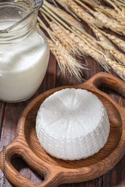 Obraz Round cottage cheese with milk and spikelets of wheat on background on a wooden table.