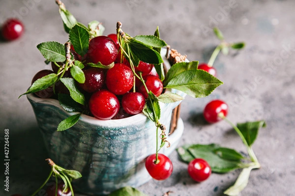 Obraz Fresh cherries with leaves and water droplets in a ceramic cup.