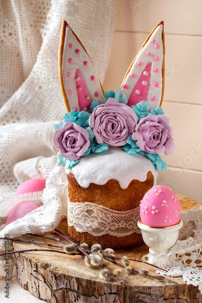 Fototapeta easter cake decorated with rabbit ears and roses meringue flowers on a light background on a wooden saw and willow branches