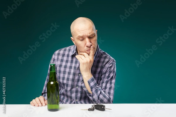 Fototapeta A man with bottle beer holds a car key and choosing ,drink alcohol or drive isolated over green background. Do not drink alcohol and drive concept.